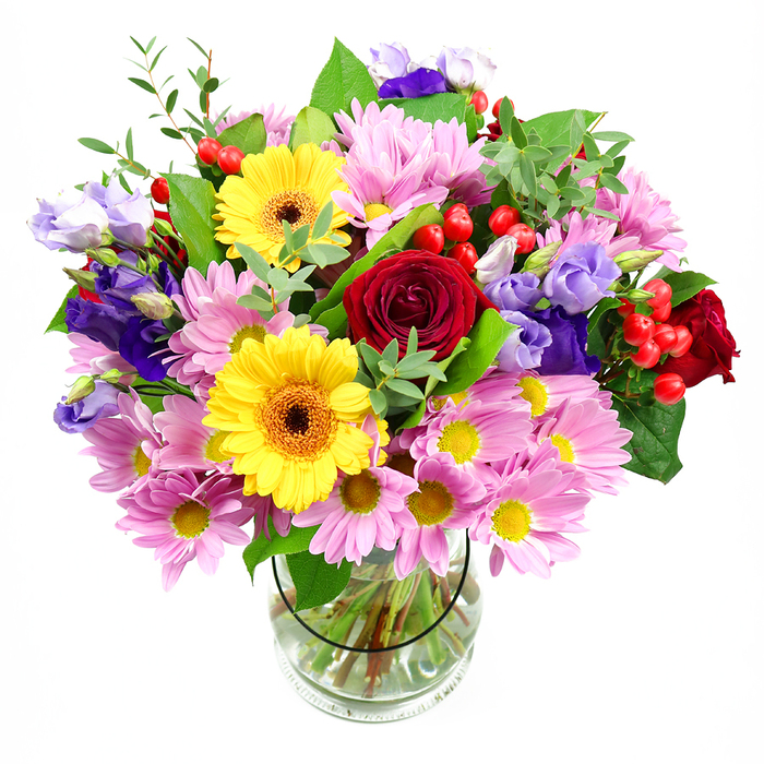 In this image, a generously proportioned bouquet overflows from a clear glass vase, set simply against a white background so that every flower can shine. At the heart of the design, plush deep red roses open luxuriously, each petal curling inward to create a velvety spiral that feels both romantic and grounding. Close by, two golden yellow gerbera daisies with dark, warm-toned centres offer a bold counterpoint, their open faces radiating friendliness and joy, much like the welcoming atmosphere of Leatherhead's local shops and cafés. Encircling these focal blooms, clusters of soft pink daisies or chrysanthemums form a broad halo, their many slender petals and dainty yellow centres combining to add volume and a light, almost cloud-like softness. Woven through this pink and yellow tapestry are elegant stems of purple and lavender lisianthus, whose elongated buds open into bell-shaped flowers with gently ruffled edges, introducing cooler hues and a graceful vertical movement. Bright red hypericum berries are scattered thoughtfully throughout the arrangement, their smooth, rounded shapes contributing playful dots of colour and a contemporary feel. The entire bouquet is supported by an array of greenery: broad, dark leaves lend strength and structure, while thinner, brighter green shoots extend outward, softening the silhouette and suggesting a freshly gathered, garden-inspired style you might associate with the leafy outskirts of Leatherhead. The clear glass vase reveals carefully trimmed stems resting in fresh water, a testament to the florist's meticulous preparation. Together, the colours, textures, and shapes create a joyous yet elegant composition, ideal as a centrepiece for a family celebration in Leatherhead or as a heartfelt gift delivered to a home near the River Mole.