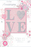 This close-up view of an anniversary card reveals a design that blends softness and elegance, much like a thoughtfully arranged bouquet delivered in Leatherhead. The central focus is the word LOVE, written in tall, refined letters that have been raised from the card's surface and brushed with delicate glitter. The sparkle is tasteful and understated, catching the light like tiny facets of ice without ever appearing garish. Encircling the word, an array of hand-drawn blossoms and trailing vines sweeps across the card in gentle arcs. These stylised flowers, suggested in shades of blush pink, ivory and smoky grey, are detailed with fine lines and subtle shading, bringing to mind the careful artistry of a florist planning an anniversary arrangement. Hints of silver foil highlight certain petals, leaves and decorative swirls, adding a luminous quality similar to sunlight glancing off the River Mole or shimmering on wet cobblestones in Leatherhead after rain. The backdrop is a smooth field of pastel pink, soft and tranquil, which allows the raised lettering and metallic embellishments to stand out clearly. Resting within this decorative frame, a scripted anniversary message pays tribute to enduring affection, trust and shared history, its flowing letters harmonising with the surrounding curves of the artwork. The overall impression is intimate and romantic: a card that feels as tender as a whispered promise, designed to be kept and revisited, much like treasured memories of years spent together in and around Leatherhead.